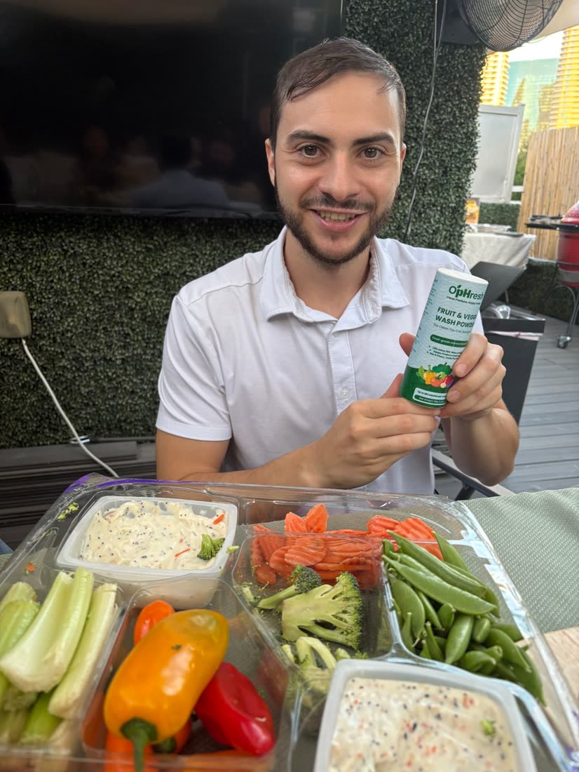 A smiling customer holding O'pHresh over a tray of fresh vegetables